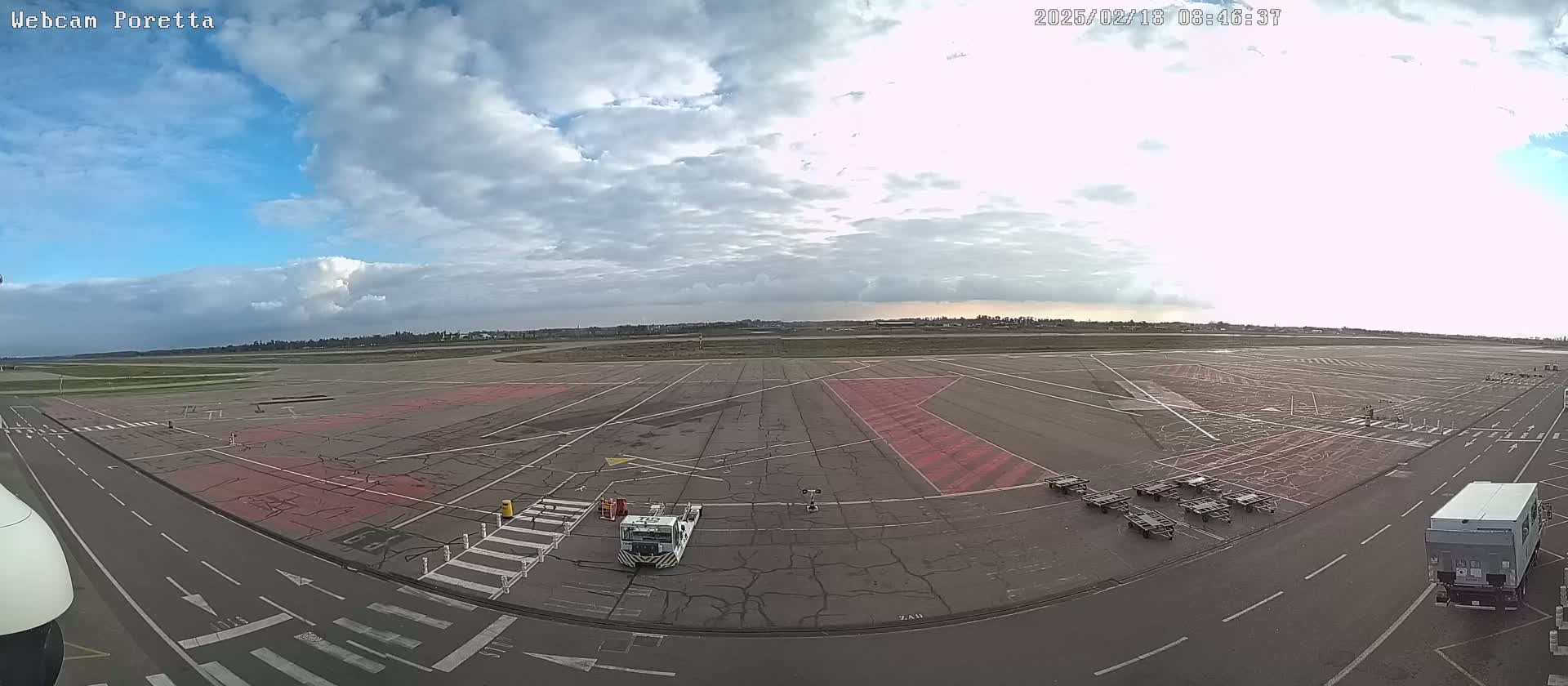 A mostly cloudy sky over a large airport tarmac with several ground support vehicles and baggage carts.