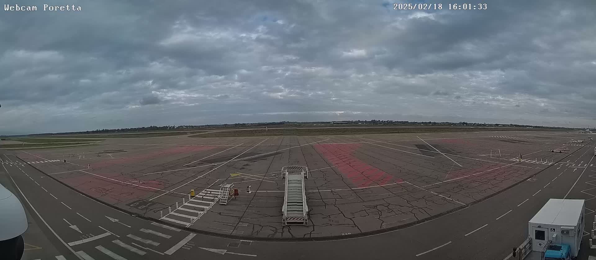 A mostly cloudy sky overlooks an airport tarmac with a jet bridge and other ground support equipment.