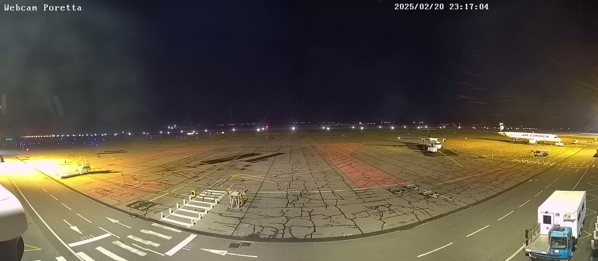 A nighttime view of an airport tarmac with several planes and ground support vehicles under a clear, dark sky.
