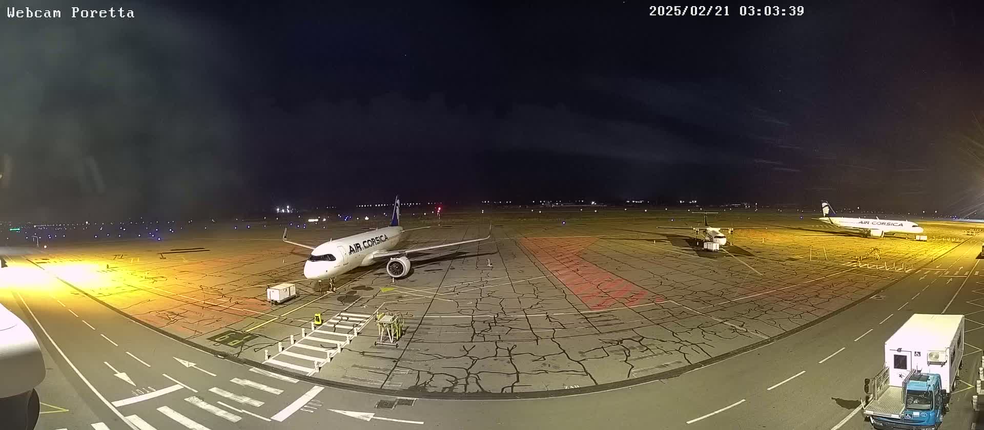 At night, two airplanes are parked on a tarmac under a mostly clear sky.