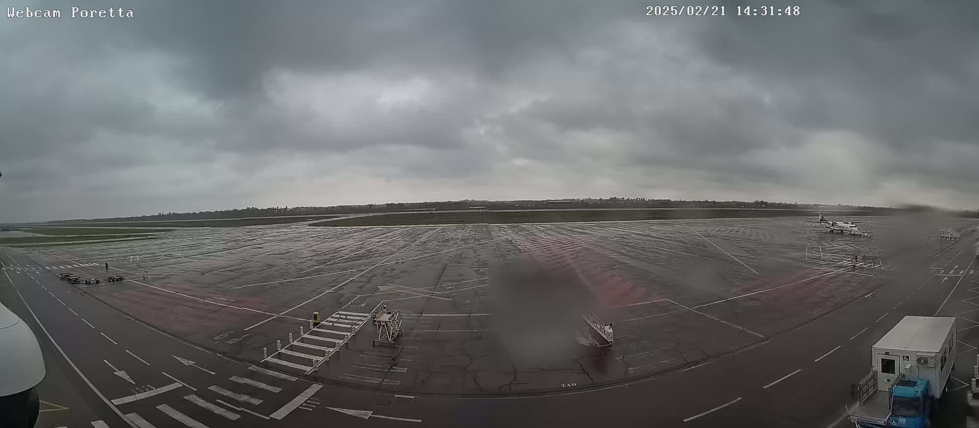 A wet airport tarmac is visible under an overcast sky, with a small plane parked on the far side.