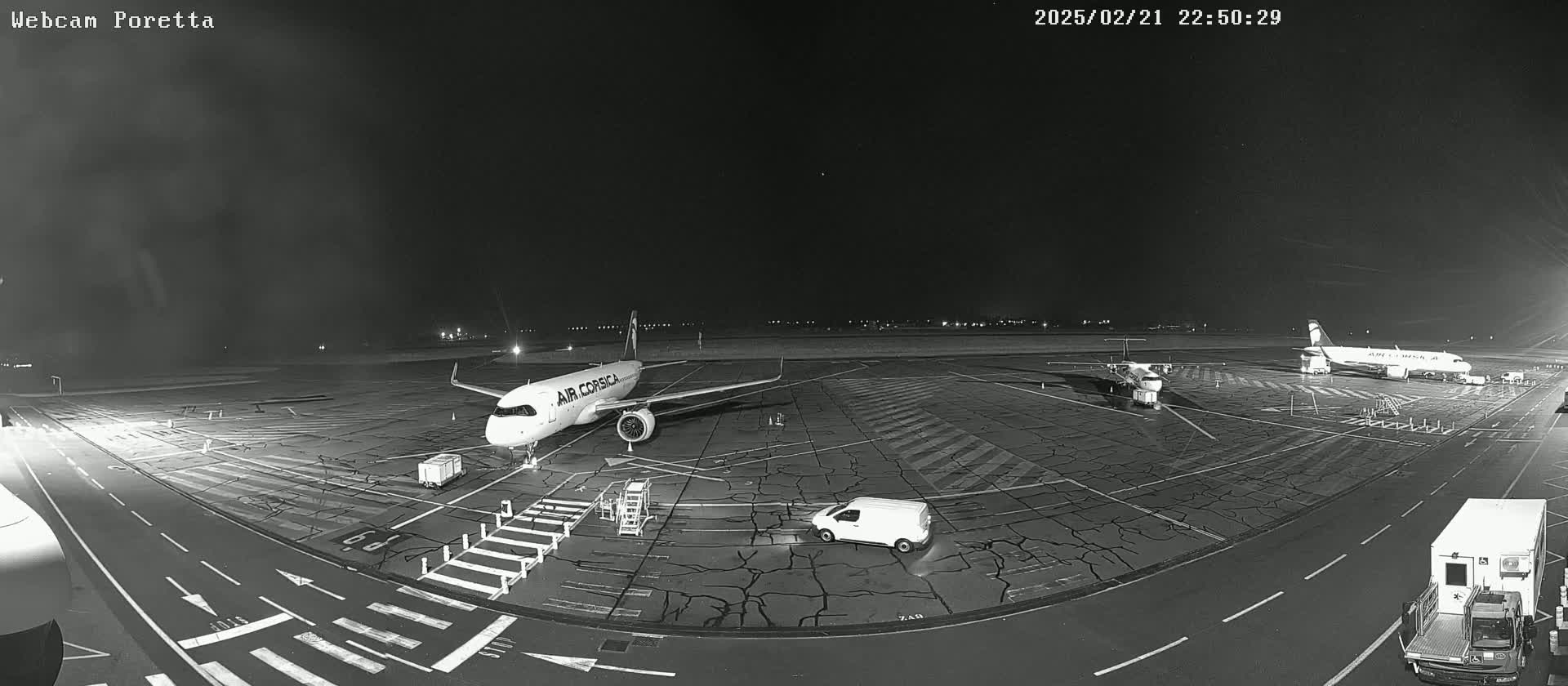 At night, an airport tarmac shows several airplanes and support vehicles under a dark sky.