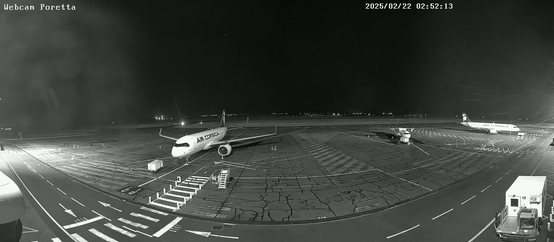 A nighttime, black and white view of an airport tarmac with several airplanes parked, one of which is an Air Corsica plane.