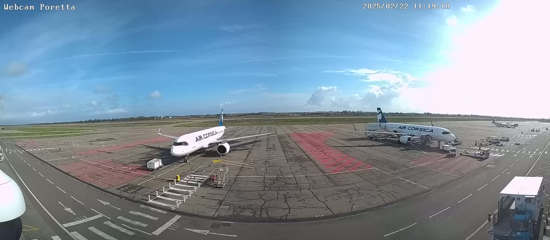 Two Air Corsica airplanes are parked on a tarmac under a mostly sunny sky with some scattered clouds.