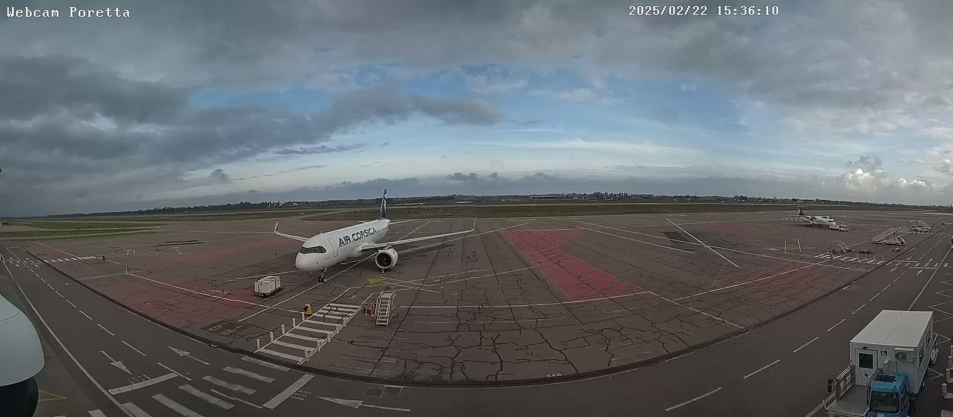 An airport tarmac under a mostly cloudy sky shows several airplanes, support vehicles, and ground markings.