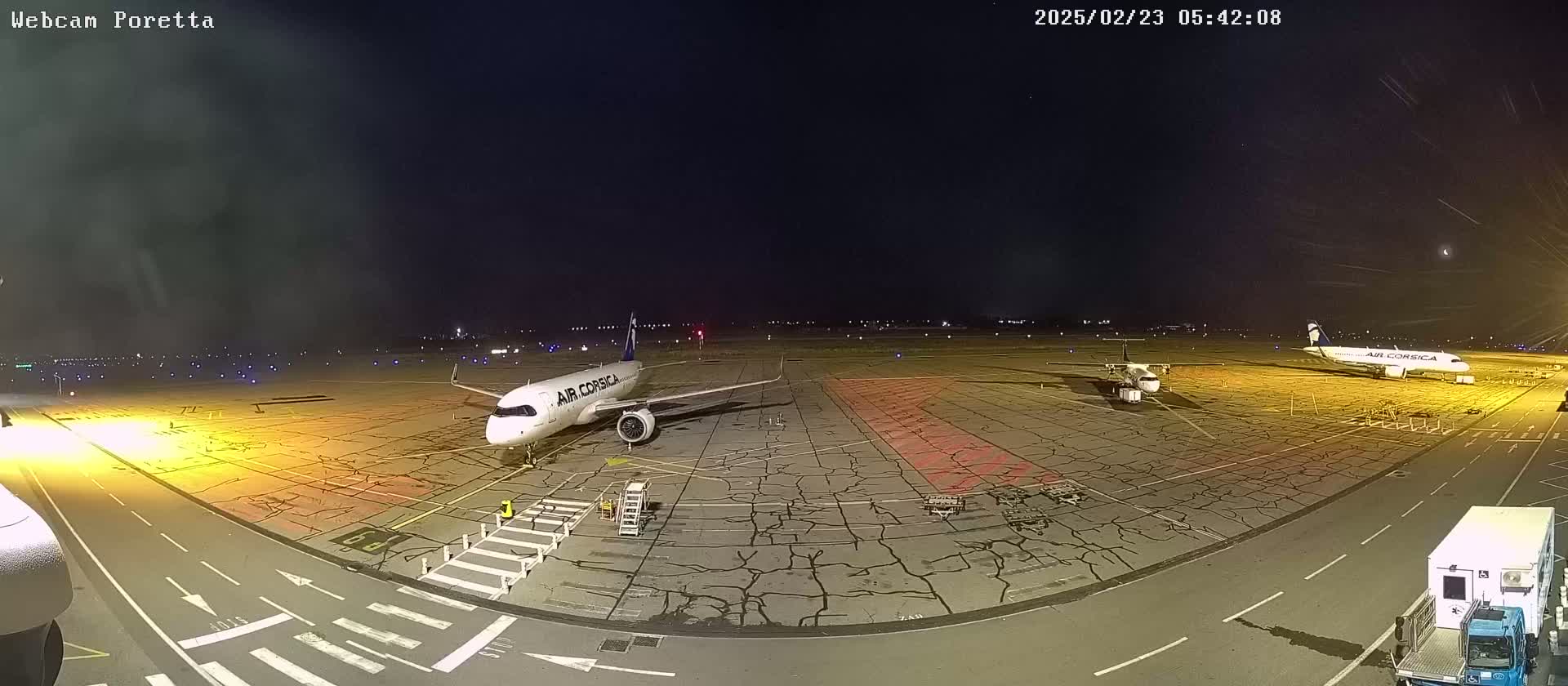 Two airplanes are parked on a tarmac at night under a dark, mostly clear sky.