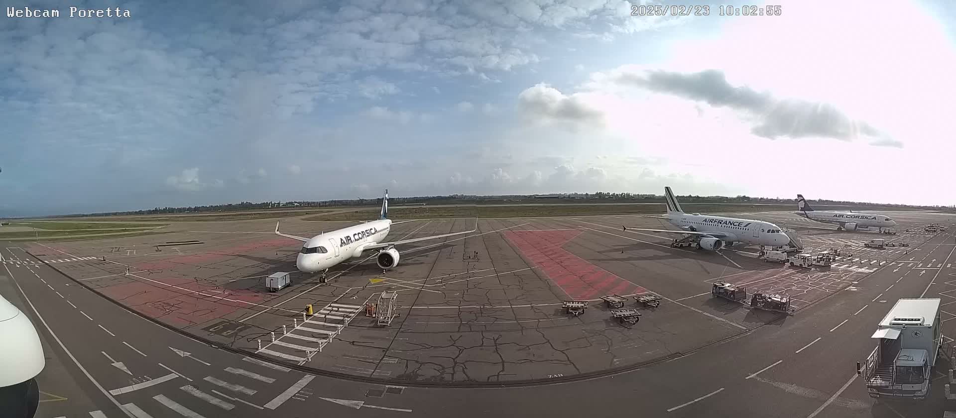 Two airplanes are parked on an airport tarmac under a partly cloudy sky.