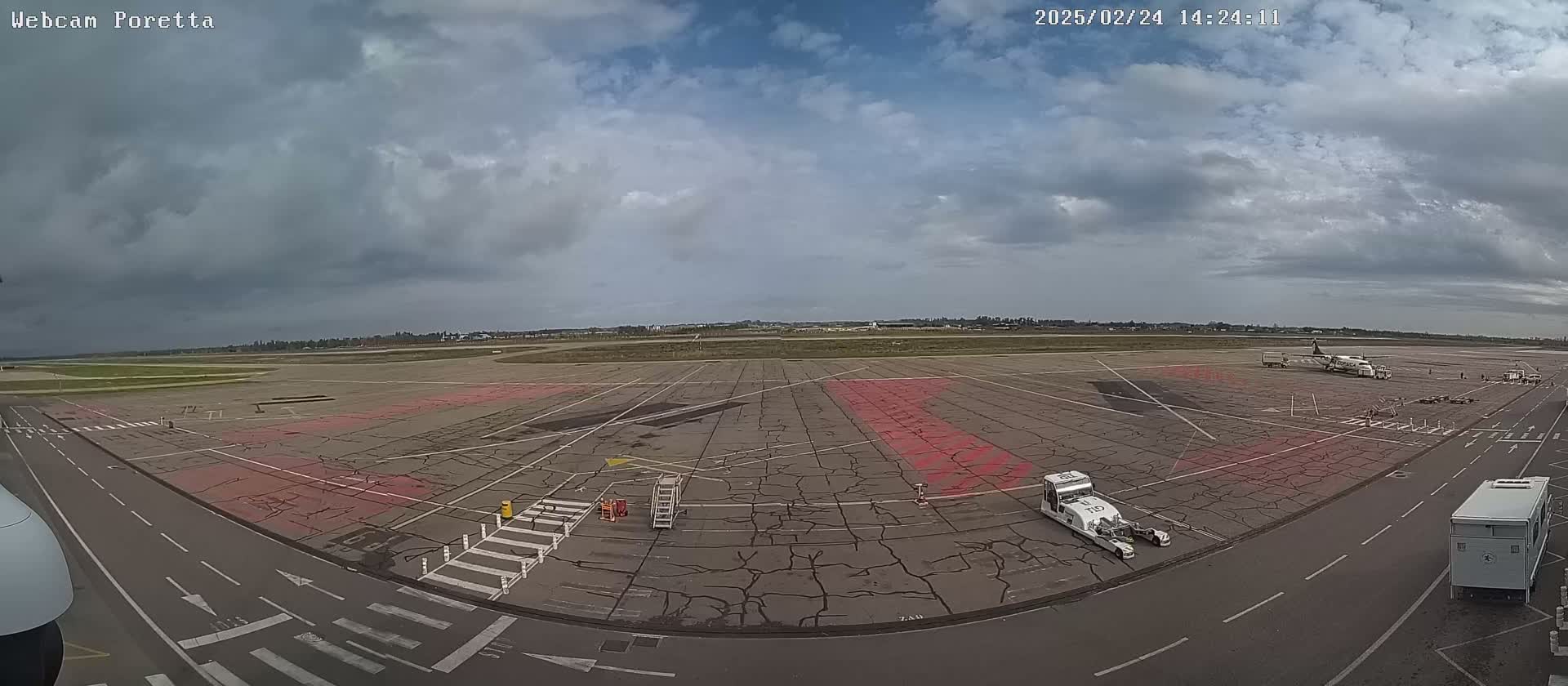 A mostly cloudy sky overlooks an airport tarmac with a plane and several ground support vehicles.