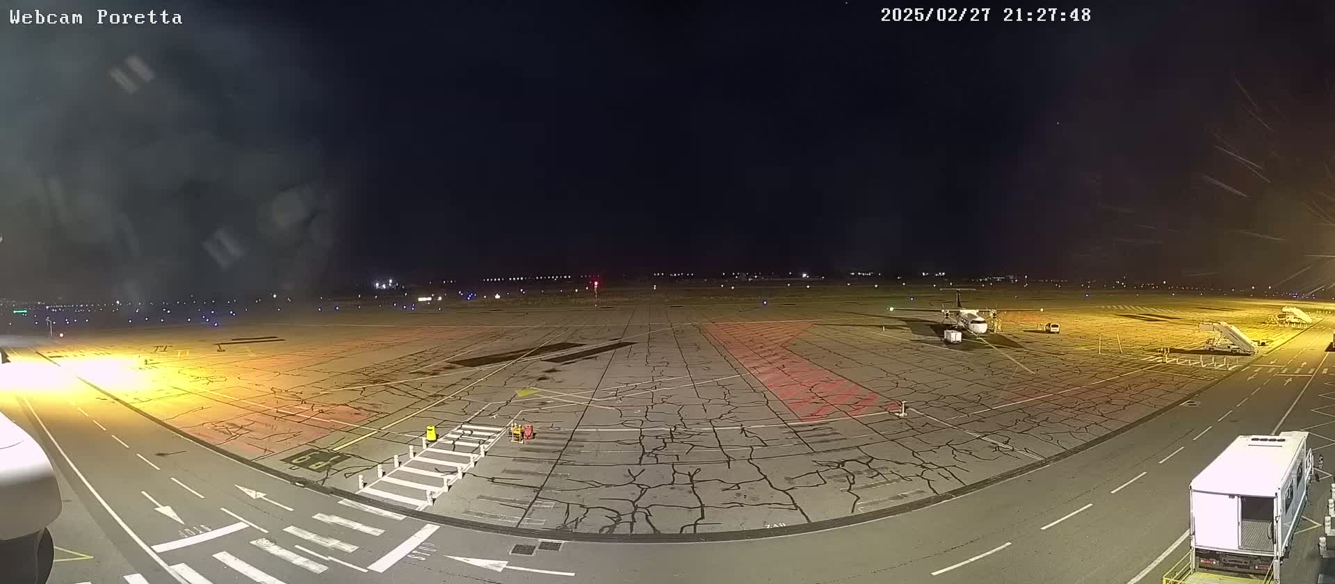A nighttime view of an airport tarmac showing a plane at a gate with ground support equipment, under a clear, dark sky.