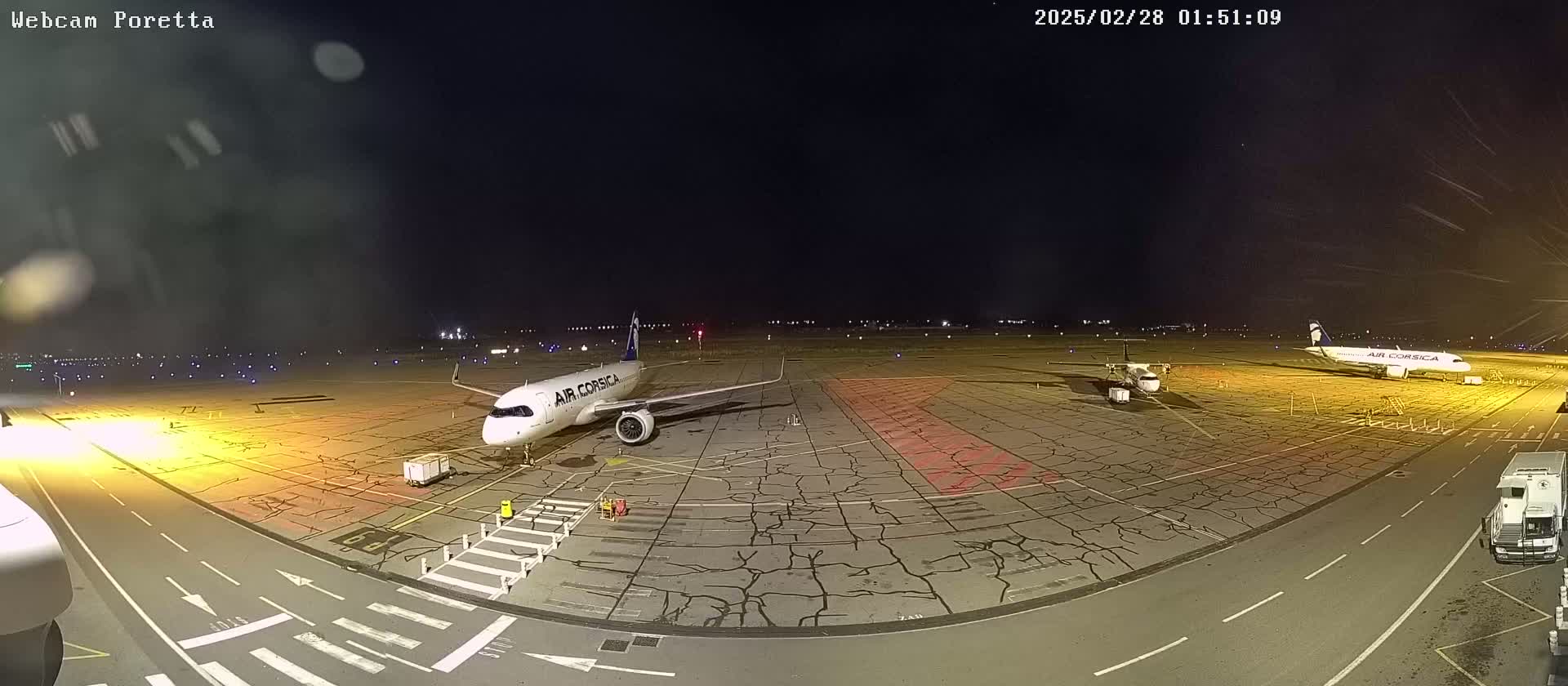 At night, two airplanes are parked on a cracked tarmac at an airport under a clear, dark sky.