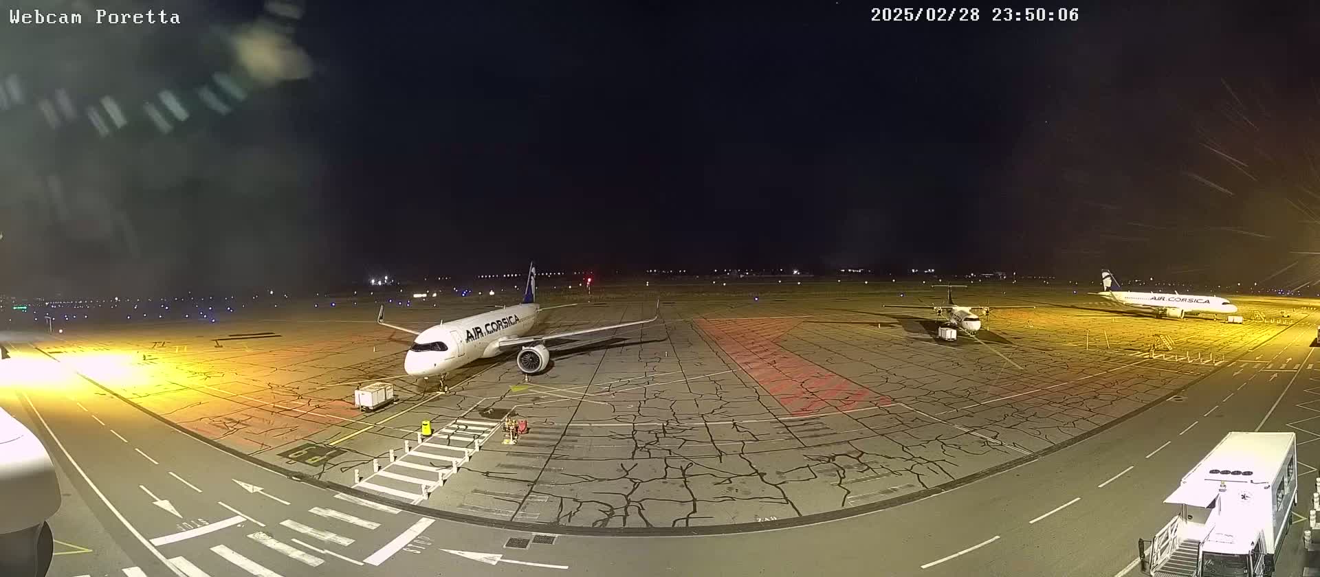 Two airplanes are parked on an airport tarmac at night, under a clear, dark sky.