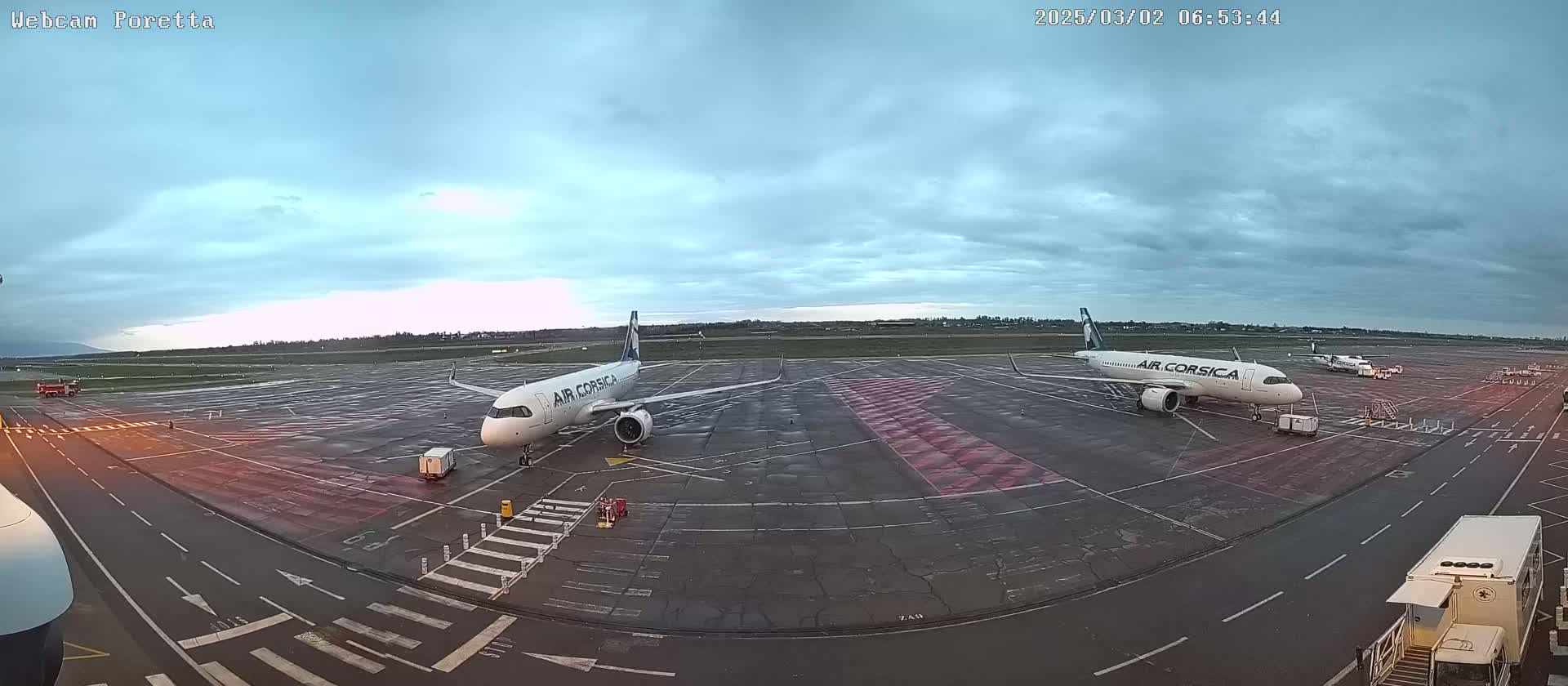 Two Air Corsica airplanes are parked on an airport tarmac under an overcast sky.