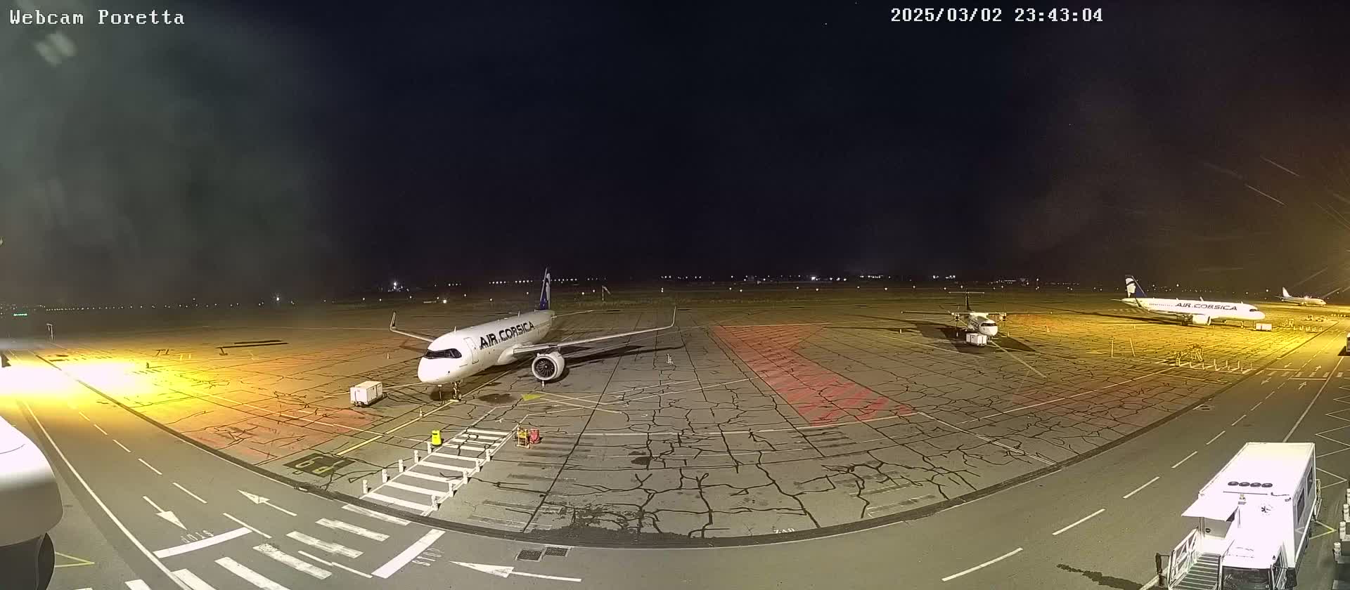 At night, two airplanes sit on a tarmac, illuminated by airport lights under a dark sky.