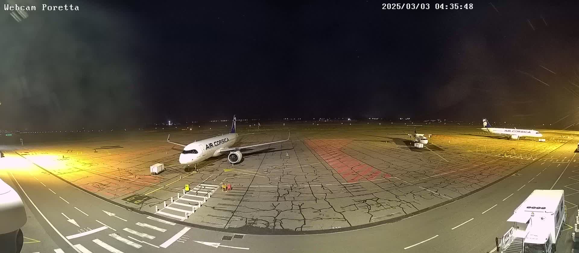 At night, two airplanes are parked on a cracked tarmac at an airport under a clear, starry sky.