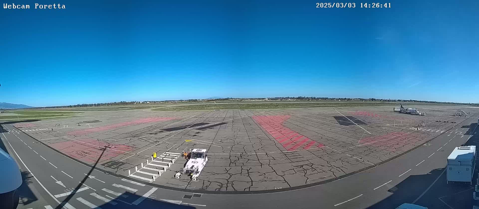 A tarmac with a cracked surface and pink markings, a small plane, and airport service vehicles is visible under a clear blue sky.