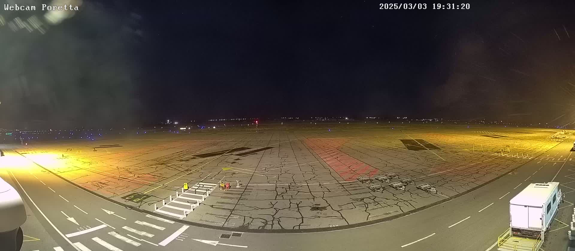 A nighttime view of an airport tarmac with several service vehicles and cracked pavement under a mostly clear sky.