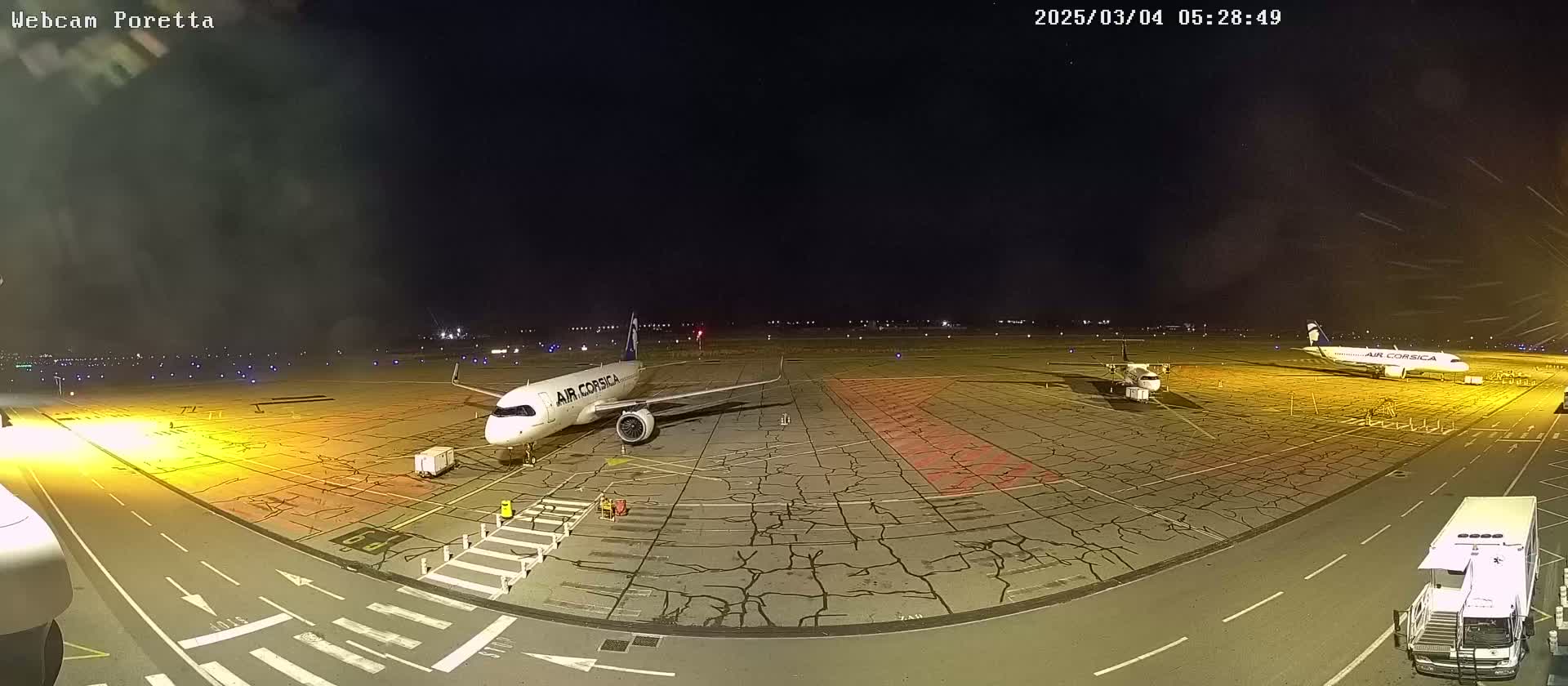 At night, two airplanes are parked on a tarmac with ground support vehicles nearby, under a clear, dark sky.