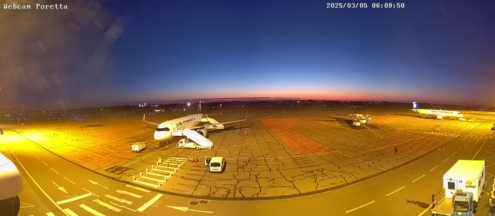 Three airplanes are parked on an airport tarmac at twilight, with service vehicles nearby.