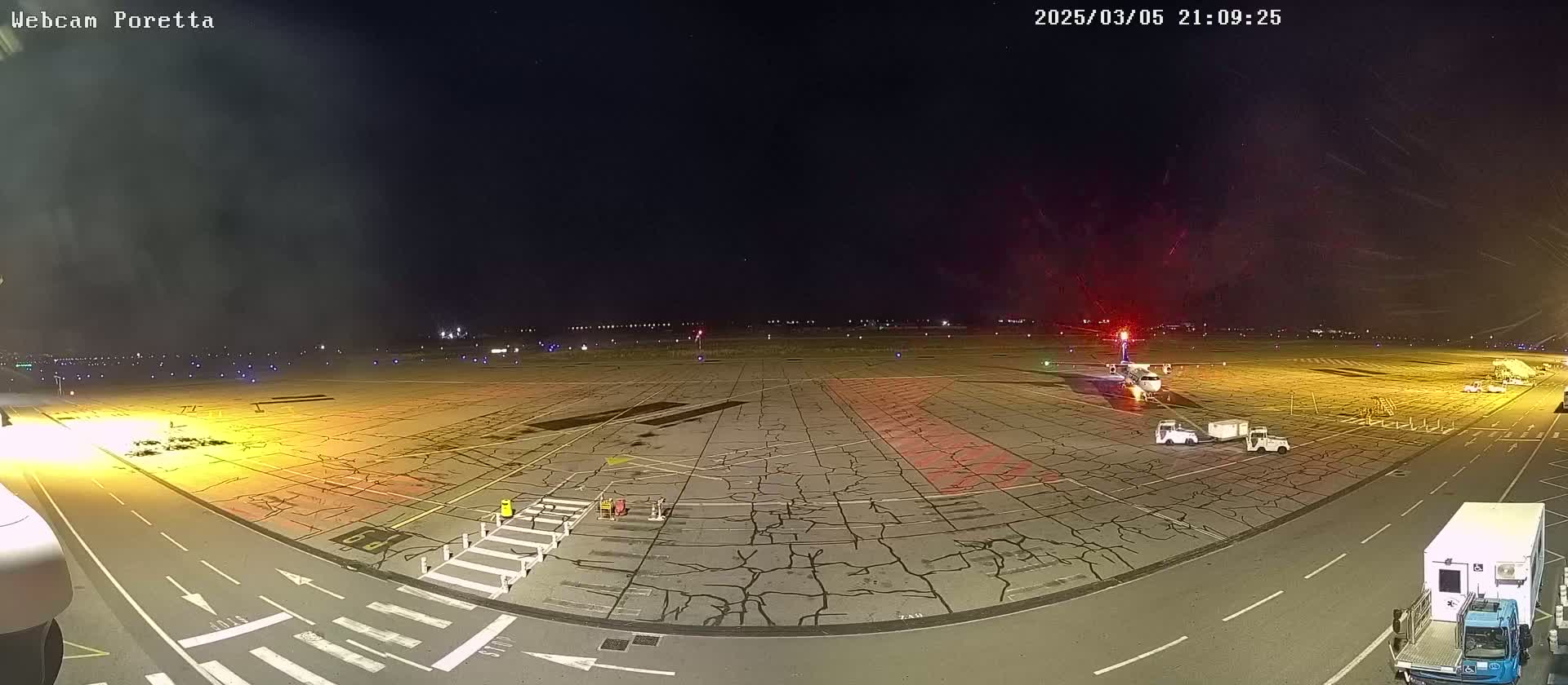 A nighttime view of an airport tarmac showing a plane parked near several ground vehicles under a clear, dark sky.
