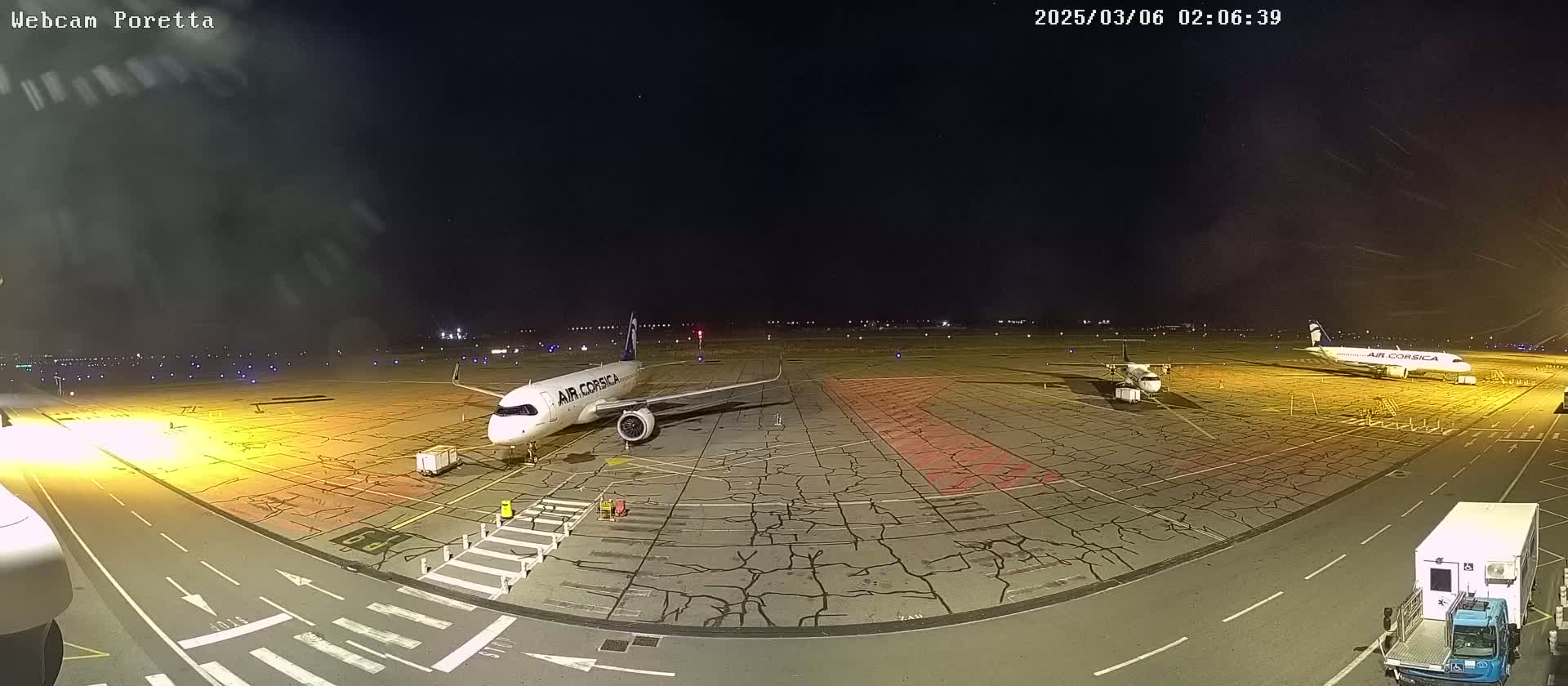 At night, under a clear, dark sky, two airplanes are parked on a tarmac with service vehicles nearby.