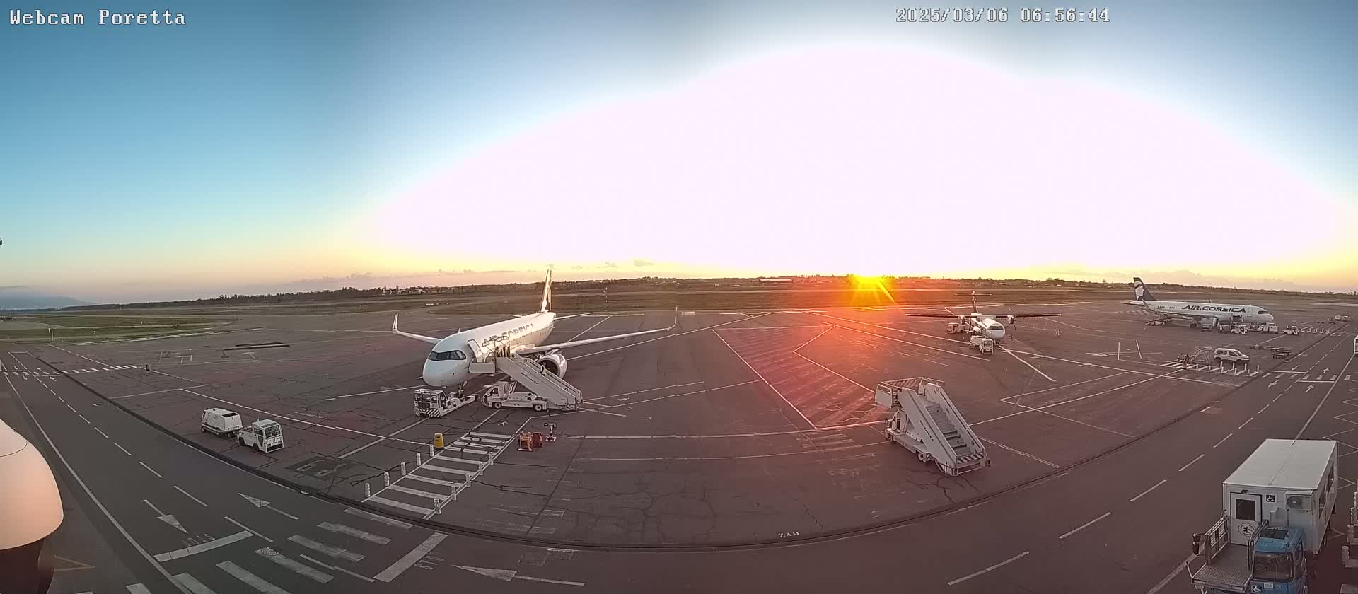 Several airplanes are parked on an airport tarmac at sunrise under a clear sky.