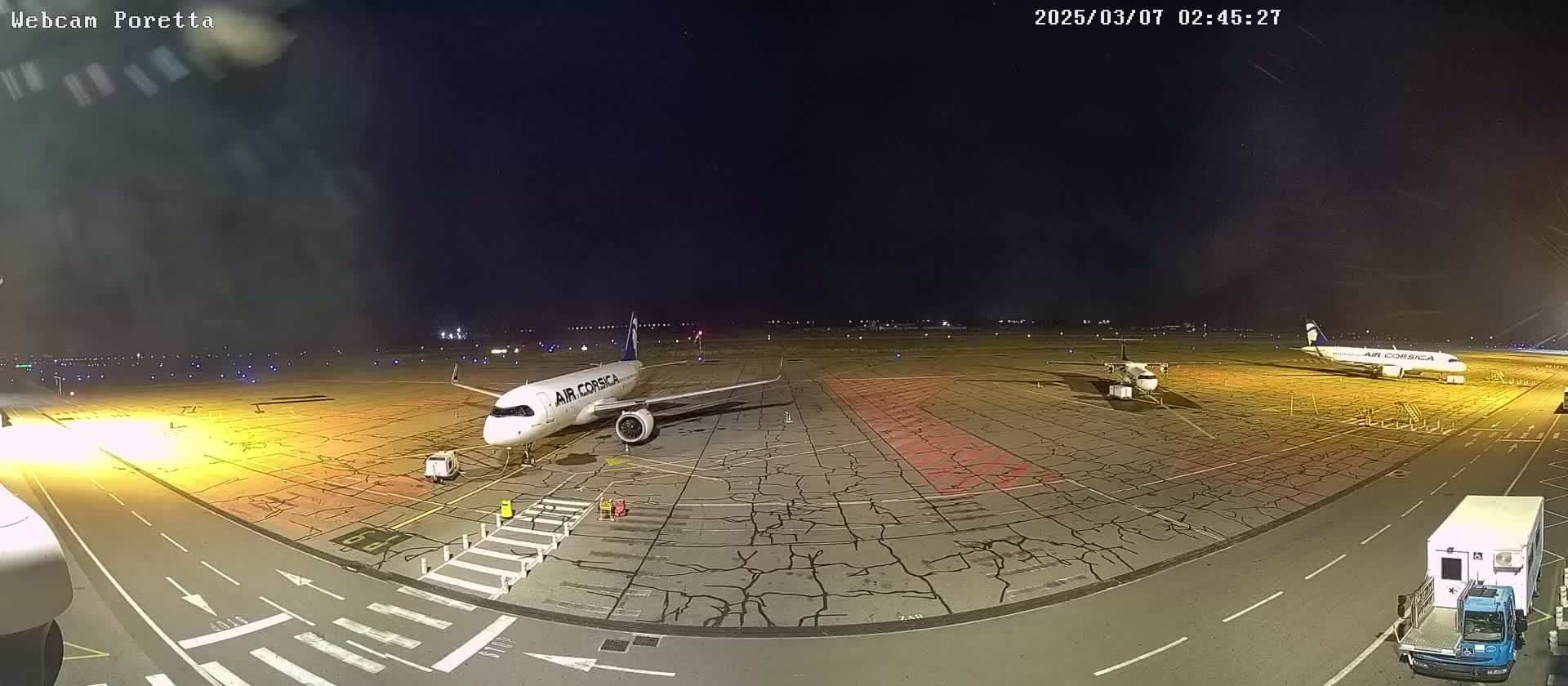 A nighttime view of an airport tarmac showing two airplanes parked, one being serviced, under a clear, dark sky.