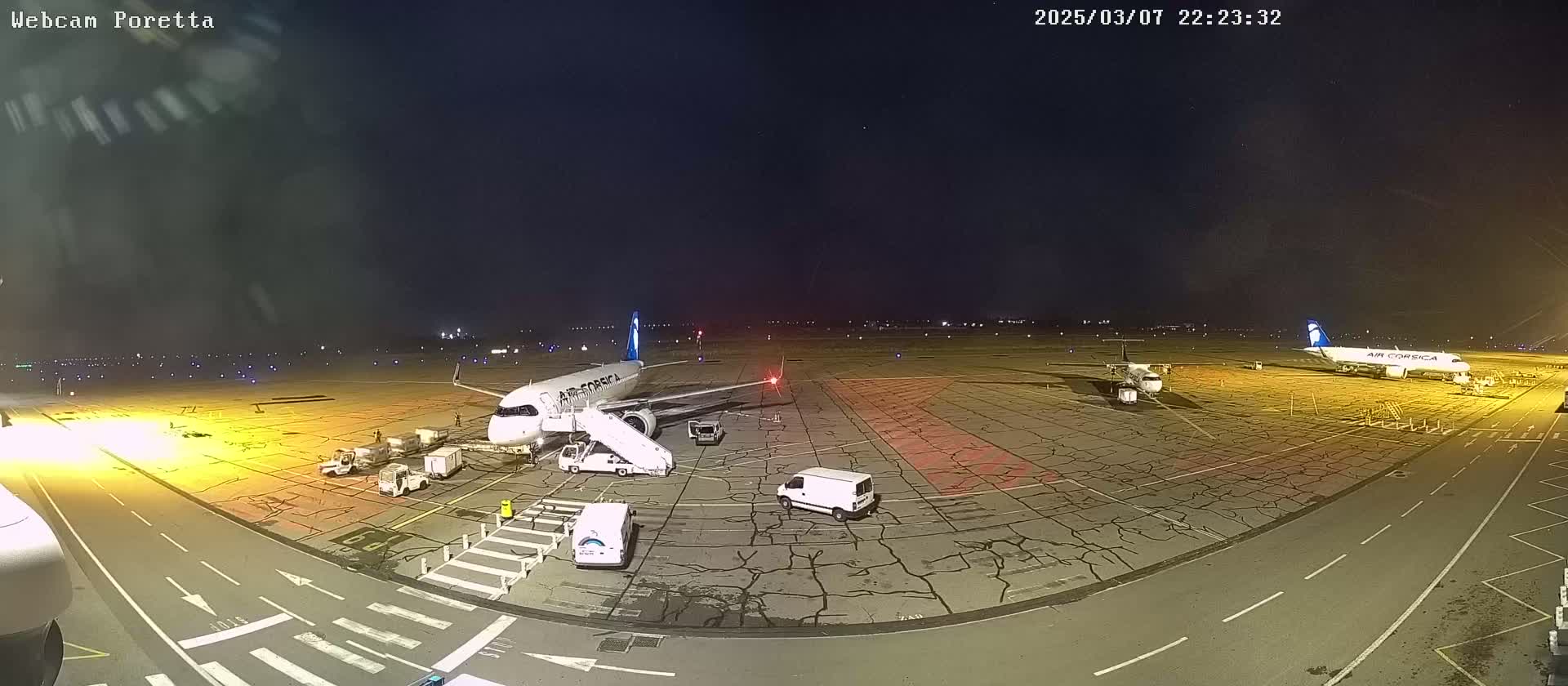At night, two airplanes are parked on an airport tarmac with service vehicles surrounding them, under a clear, dark sky.