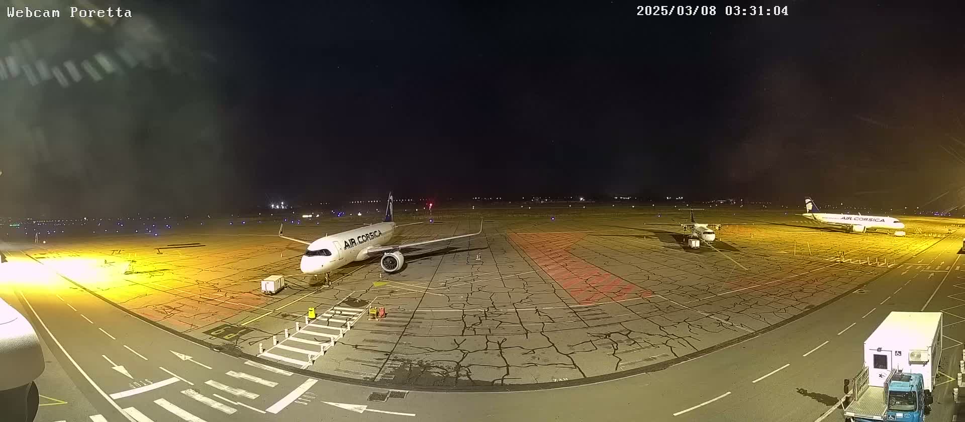 At night, on an airport tarmac with cracked pavement, two airplanes are parked; one is larger than the other.
