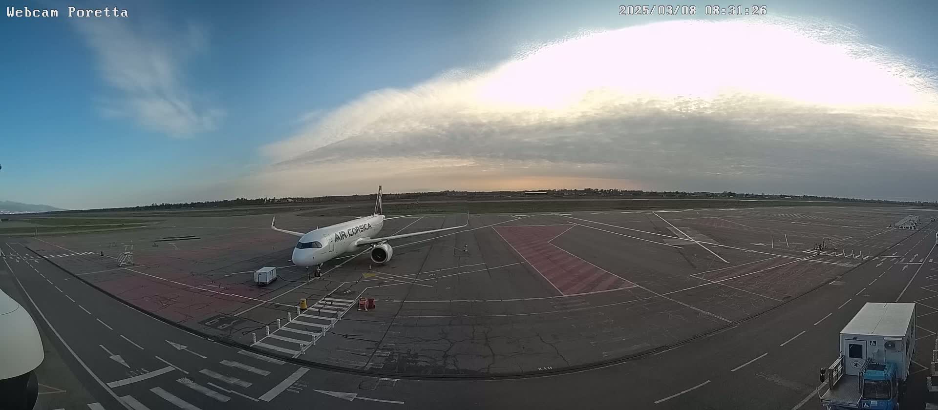A white Air Corsica airplane sits on a tarmac under a partly cloudy sky.