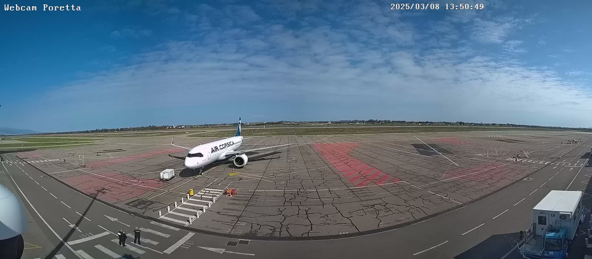 A white airplane is parked on an airport tarmac under a mostly sunny sky with a few clouds.