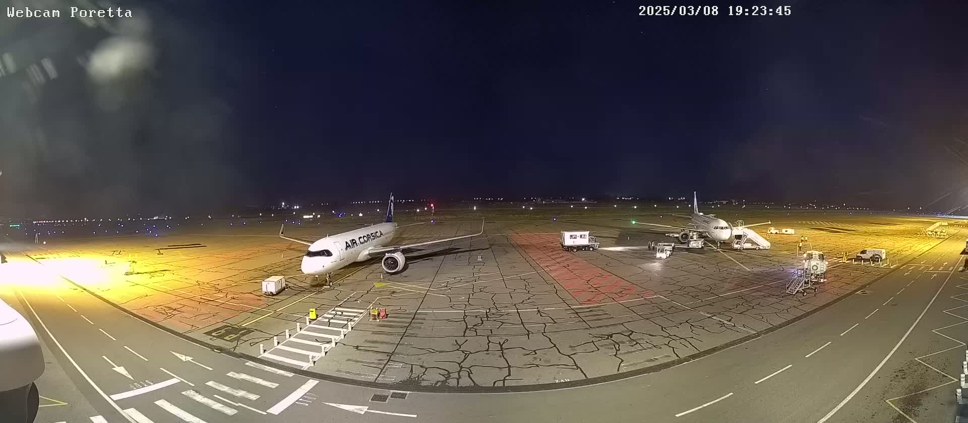 A nighttime airport tarmac view shows two airplanes parked near several support vehicles under a clear, dark sky.
