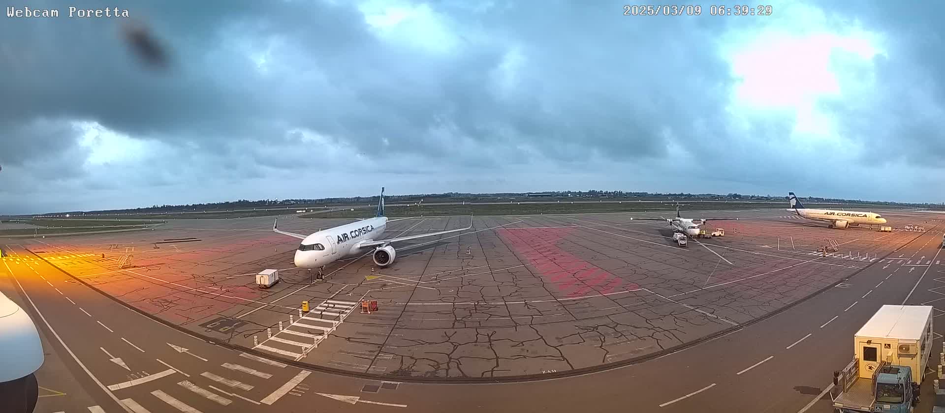 Two airplanes are parked on an airport tarmac under a cloudy sky.