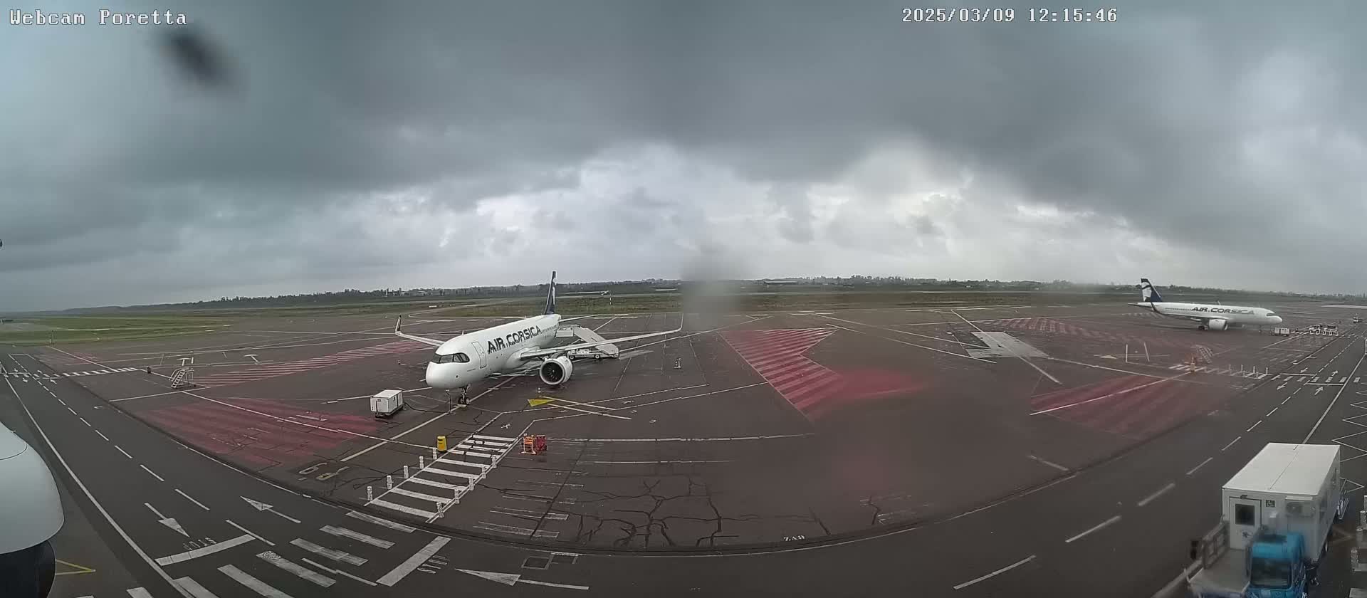 Two Air Corsica airplanes are parked on a tarmac under an overcast sky.