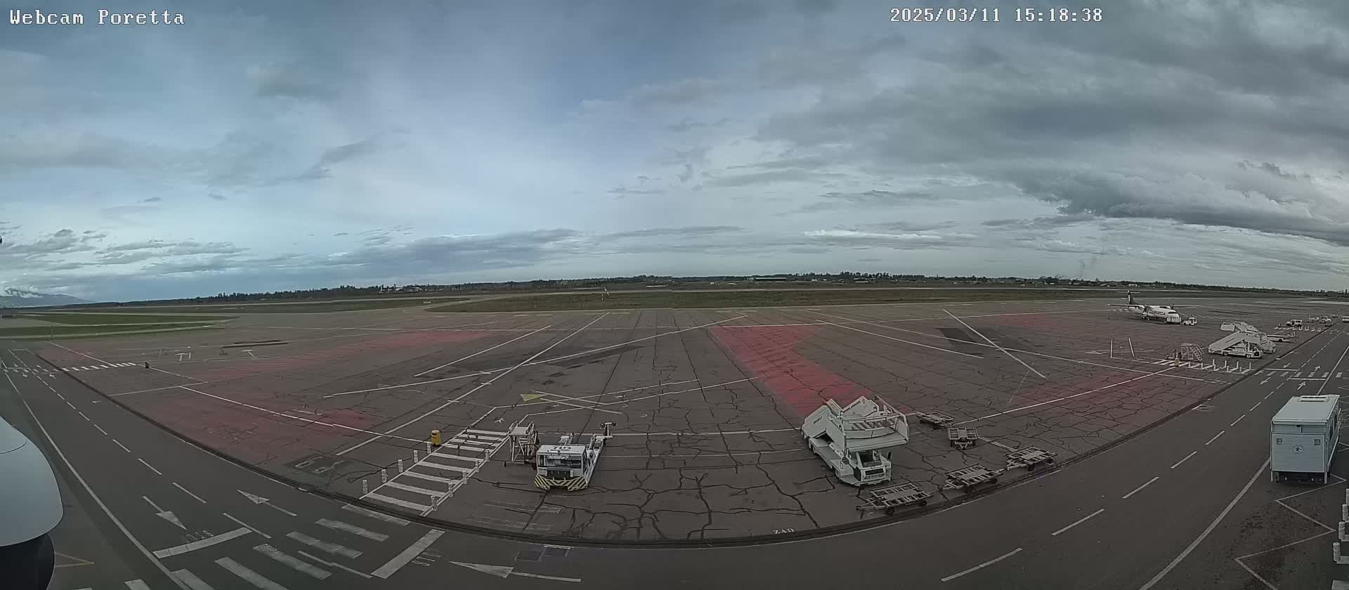 An overcast sky hangs over an airport tarmac, where several airplanes and ground support equipment are parked.