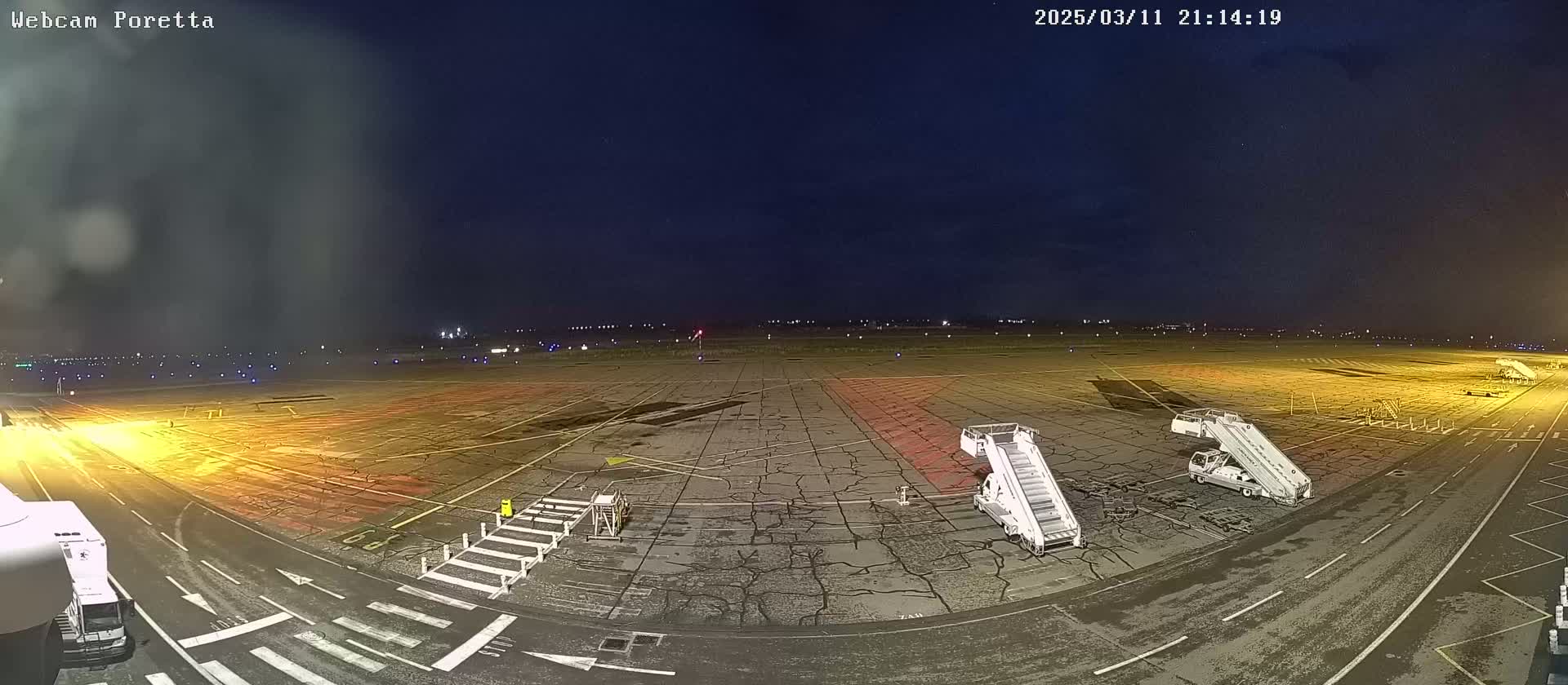 A nighttime view of an airport tarmac with jet bridges and ground support equipment, under a dark, mostly clear sky.