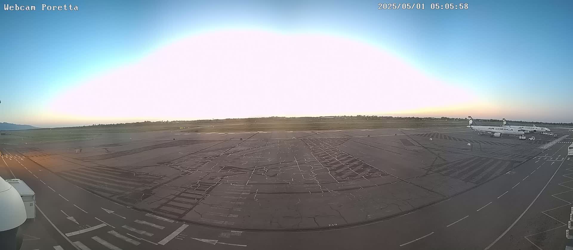 A mostly clear sunrise illuminates an airport tarmac with two airplanes parked near the terminal.