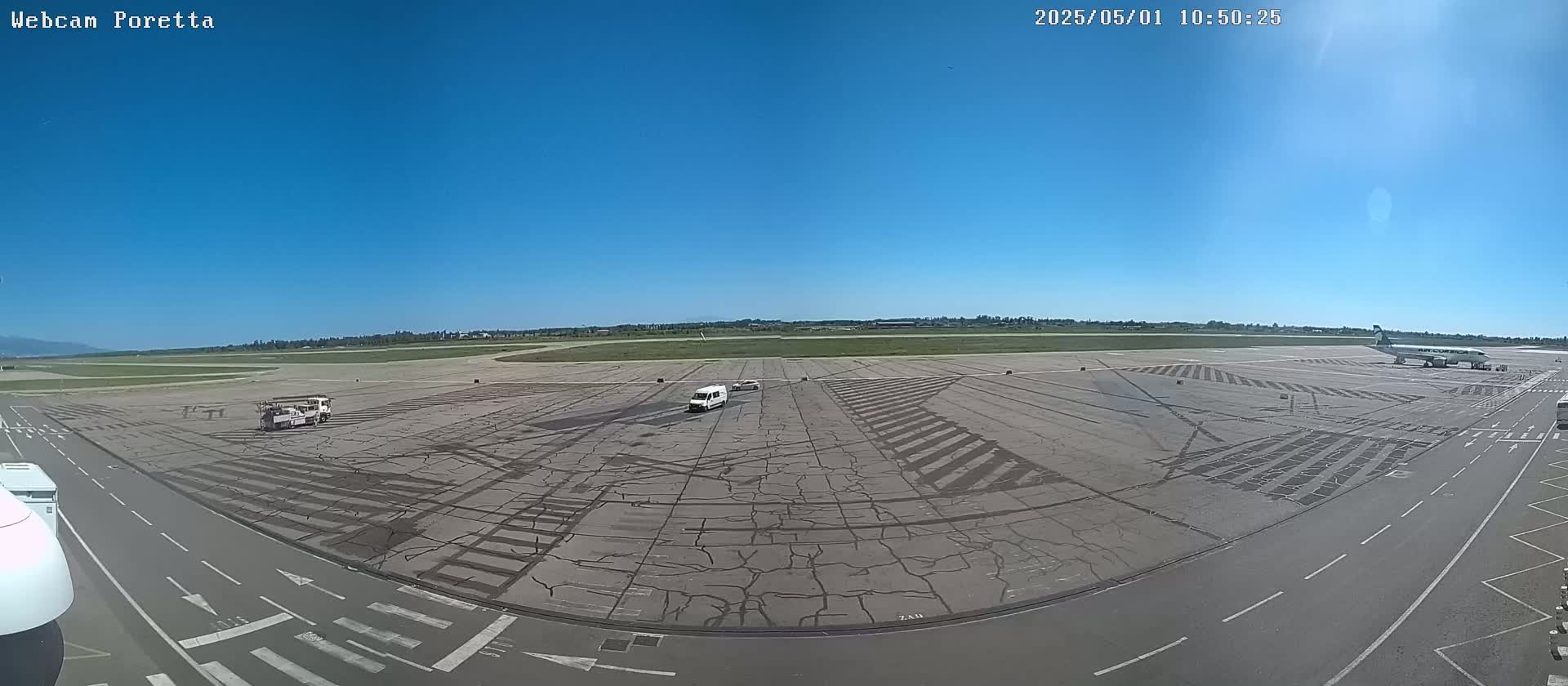 A mostly sunny airfield with several vehicles and a single airplane visible on the tarmac.