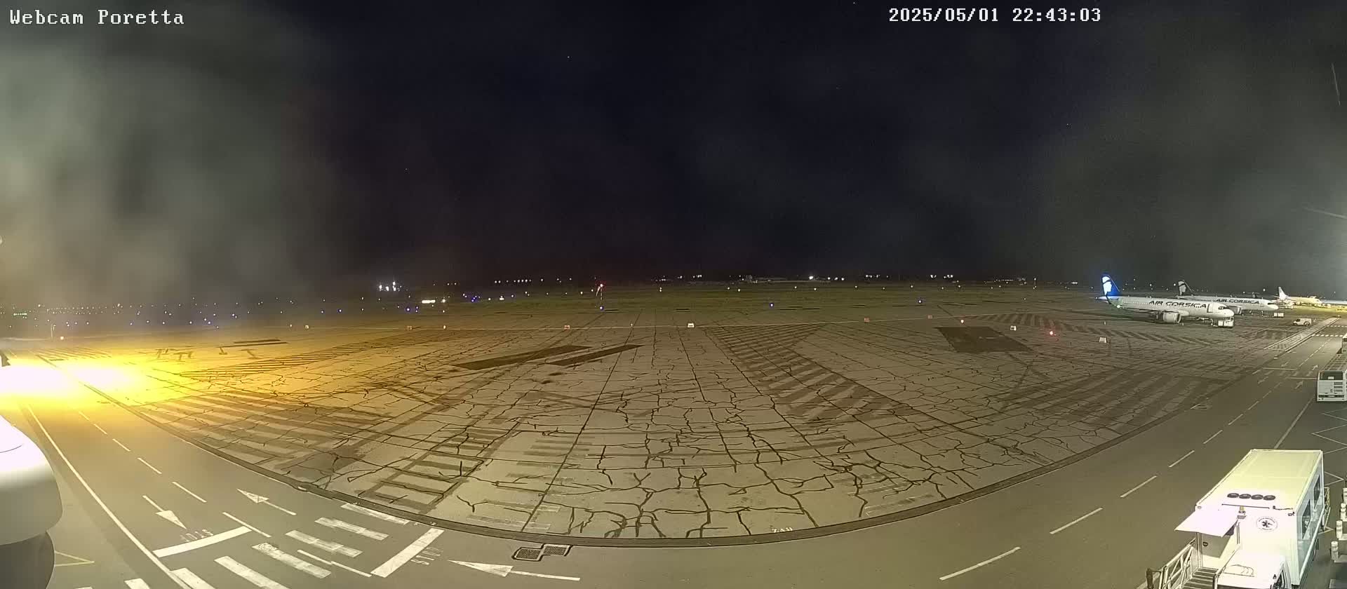 A nighttime view of an airport tarmac with two airplanes parked, under a hazy, dark sky.