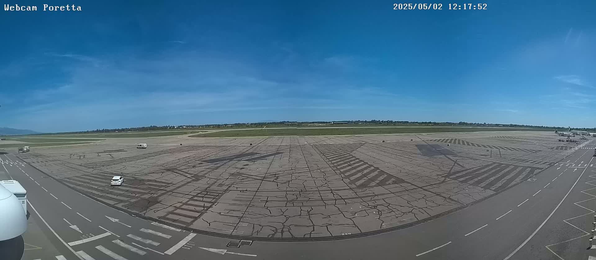 A mostly sunny day at an airport tarmac shows cracked pavement with painted markings and a few vehicles.