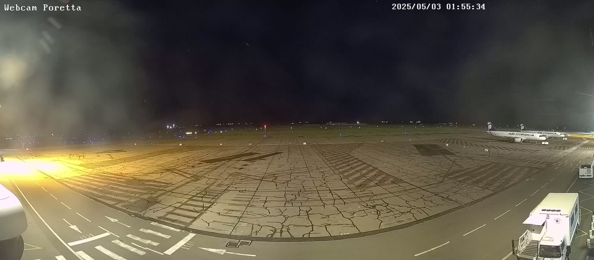 A nighttime view of an airport tarmac with two airplanes parked, showing a cracked surface and some ground support equipment.