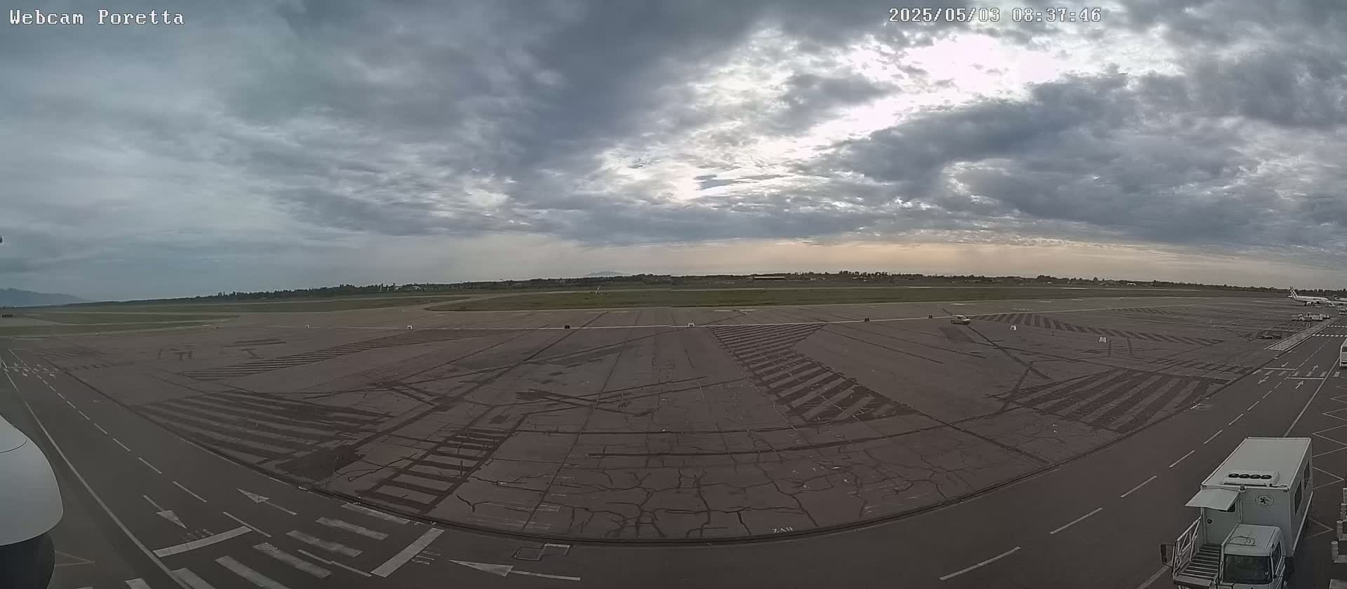 An overcast sky hangs over an empty airport tarmac with a few vehicles visible.