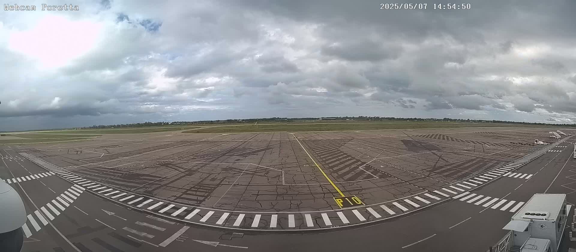 A mostly cloudy sky overlooks an airport tarmac with various markings and a few service vehicles.