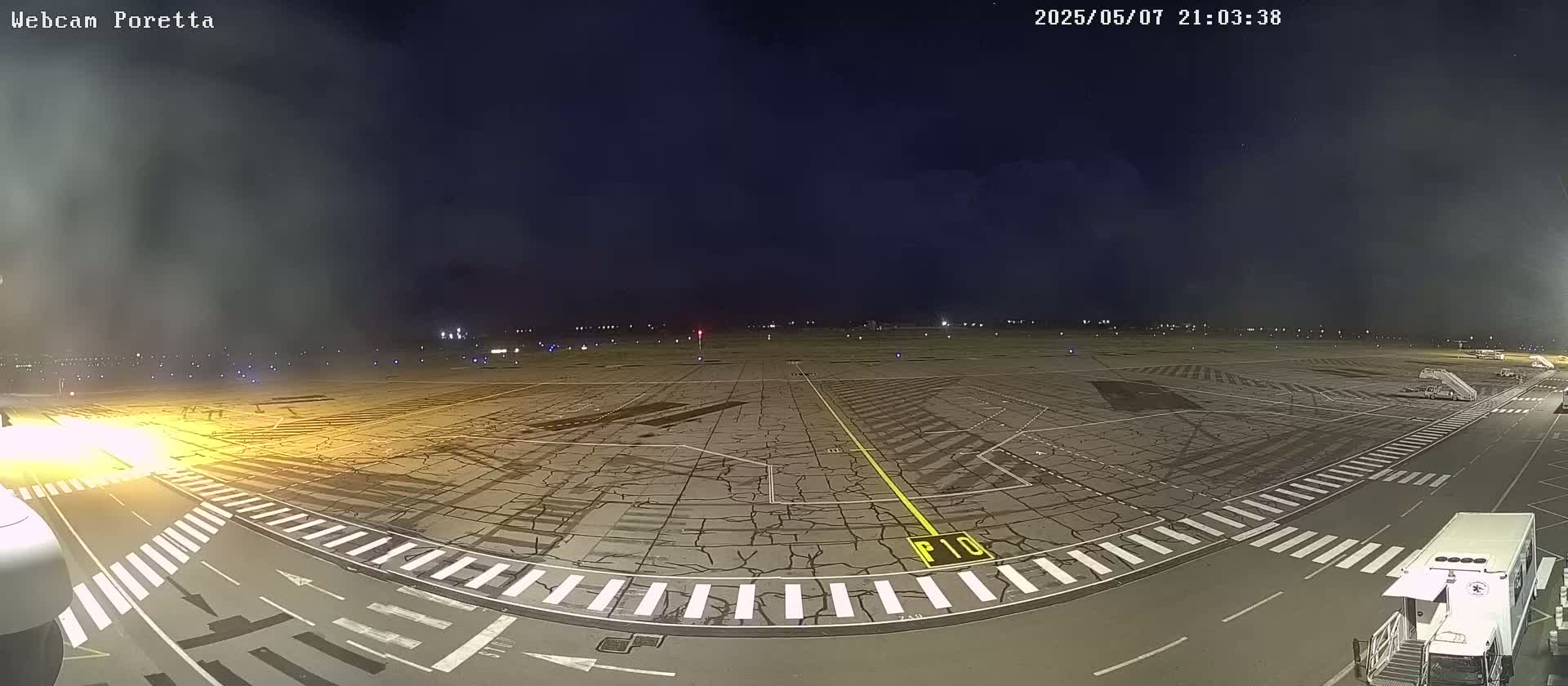 A nighttime view of an airport tarmac showing cracked pavement, taxiways, and ground support equipment under a mostly clear, dark sky.
