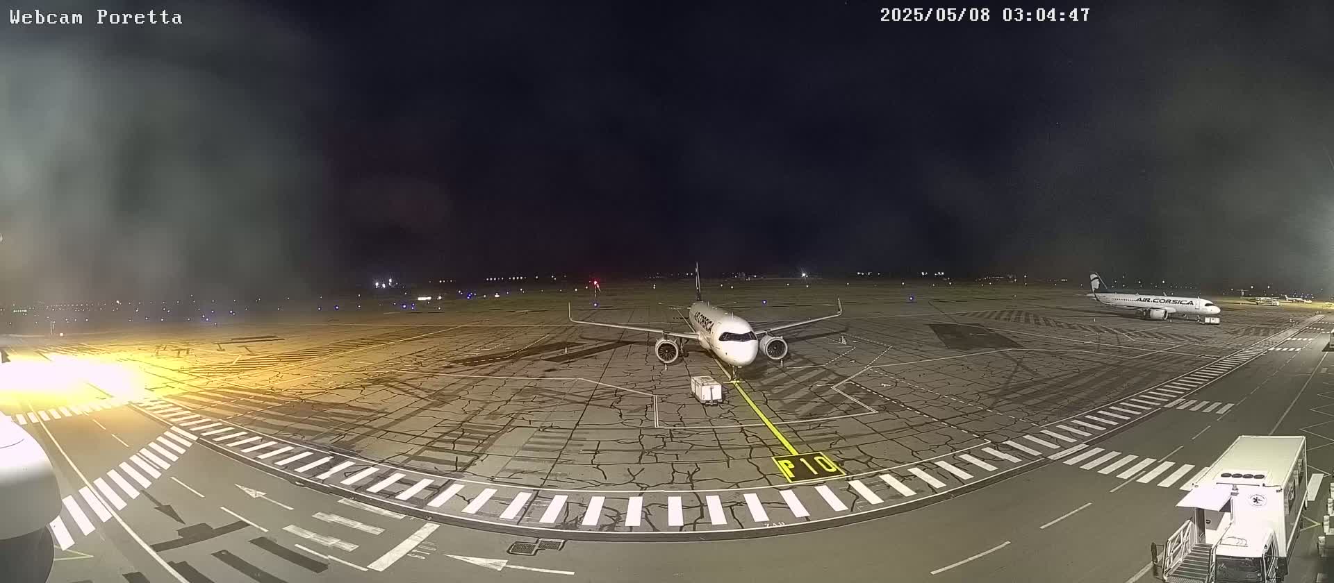 A passenger airplane sits on an airport tarmac at night under a dark, hazy sky.
