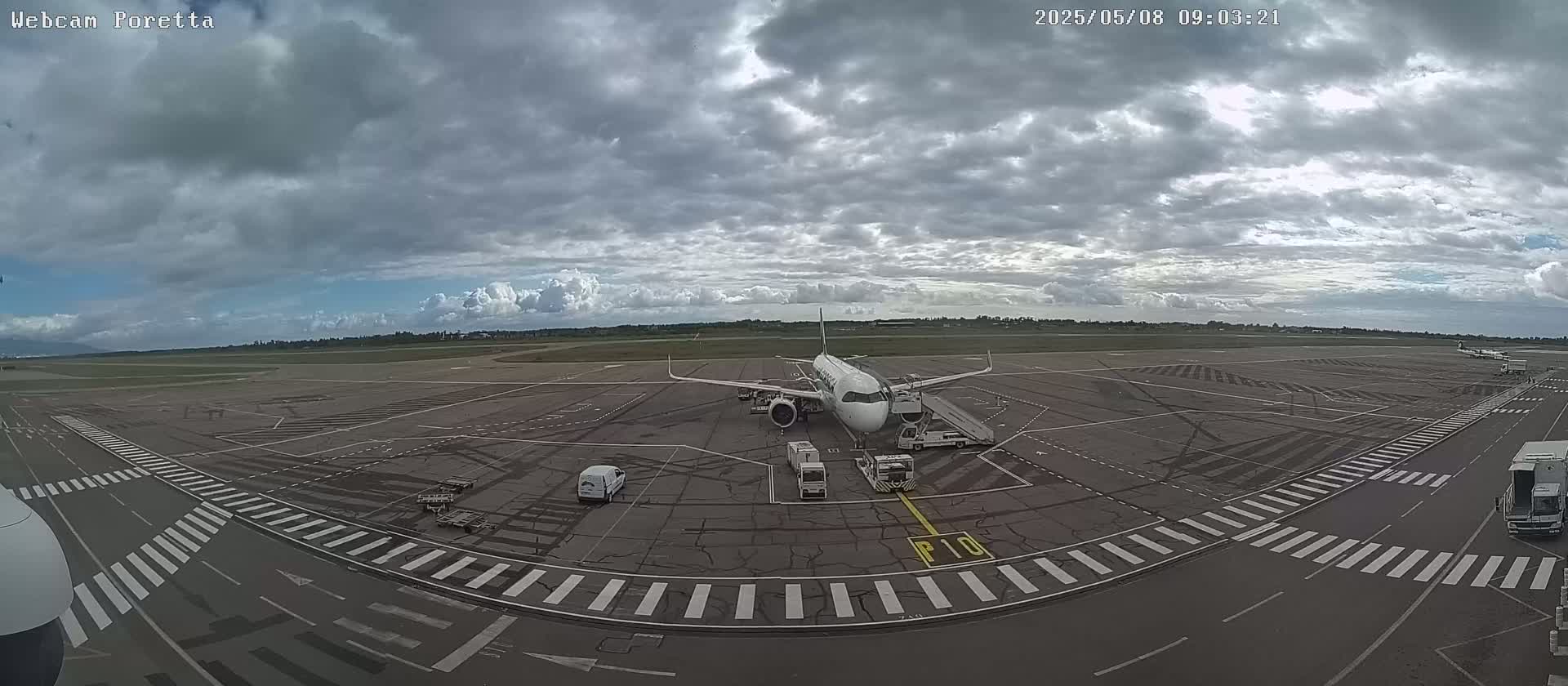 A passenger airplane is parked on an airport tarmac under a mostly cloudy sky.