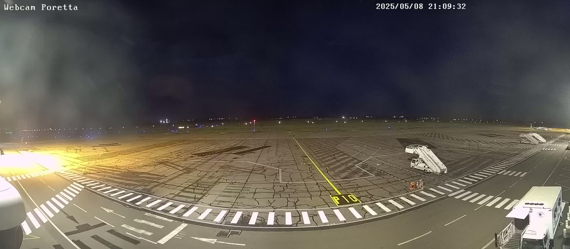 A nighttime view of an airport tarmac with several jet bridges and ground support vehicles, under a dark, slightly hazy sky.