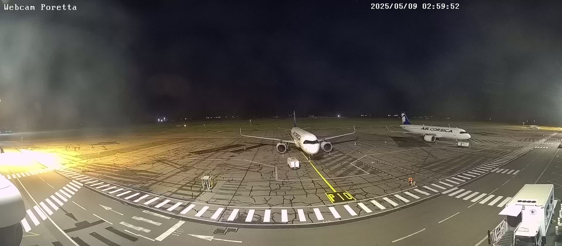 At night, two airplanes are parked on a tarmac, with one closer to the camera than the other.