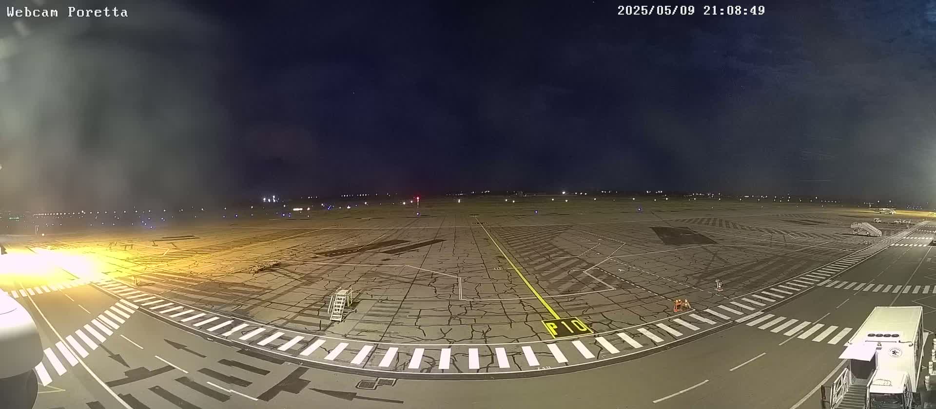 A nighttime view of an airport tarmac with several vehicles and jet bridges, under a mostly clear, dark sky.