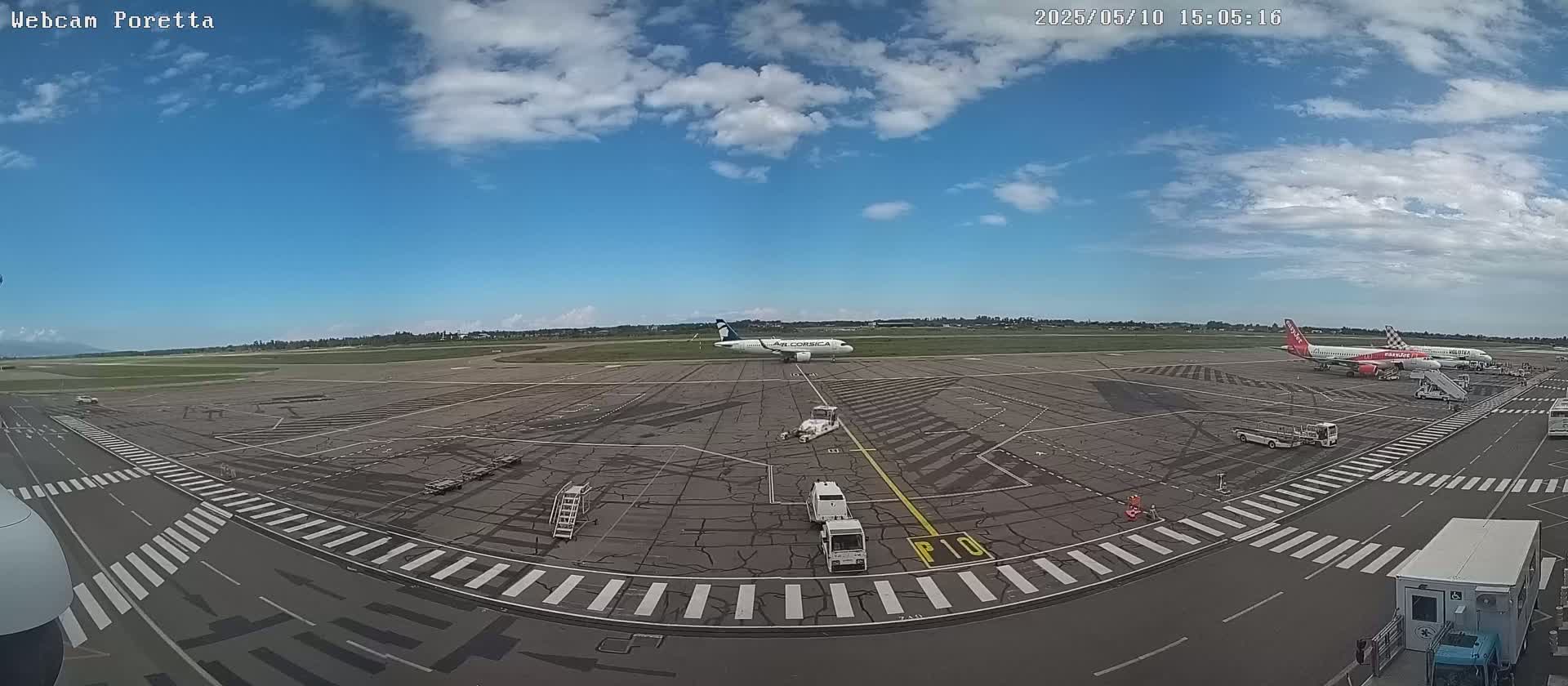 An airport tarmac under a partly cloudy sky shows several airplanes and ground support vehicles.