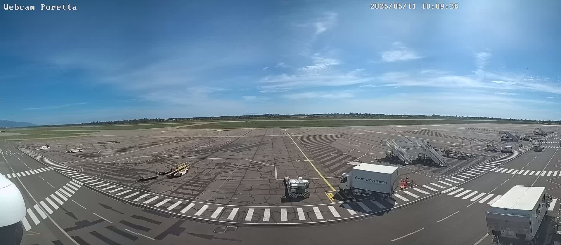 A tarmac at an airport on a sunny day with several service vehicles and jet bridges.